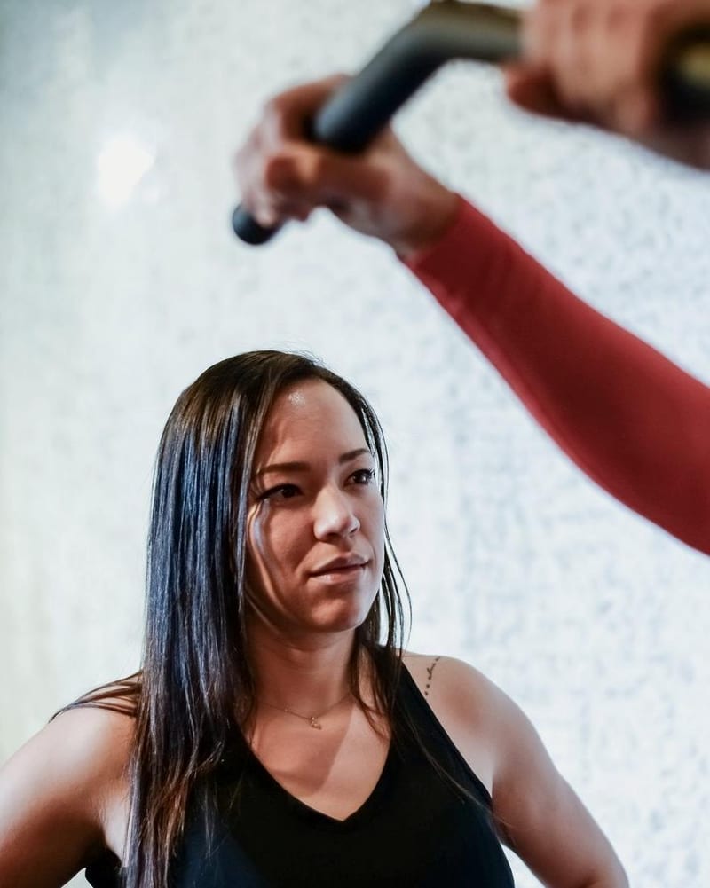 A woman in a black vest watches a client on gym equipment